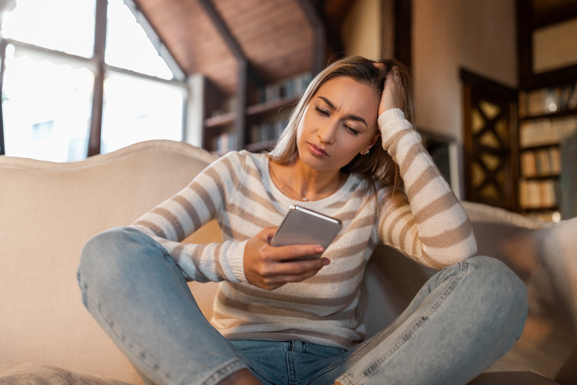 Confused woman looking at phone, head resting on her hand.