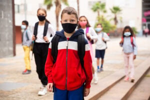 Group of children in protective masks walking to school campus after lessons