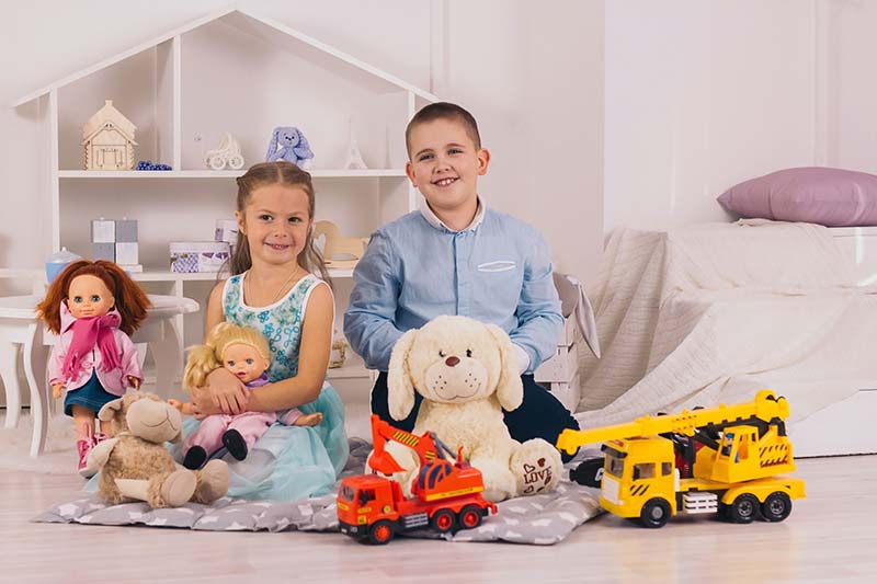 beautiful happy caucasian children sitting in their room, boy with car, girl with doll