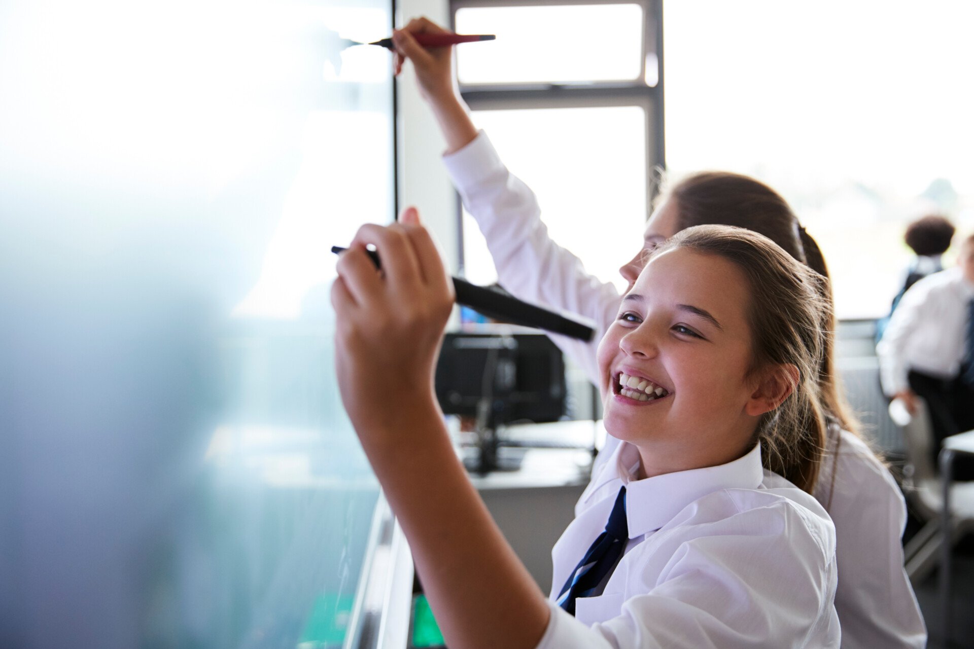 Two young students smiling and using an interactive whiteboard.