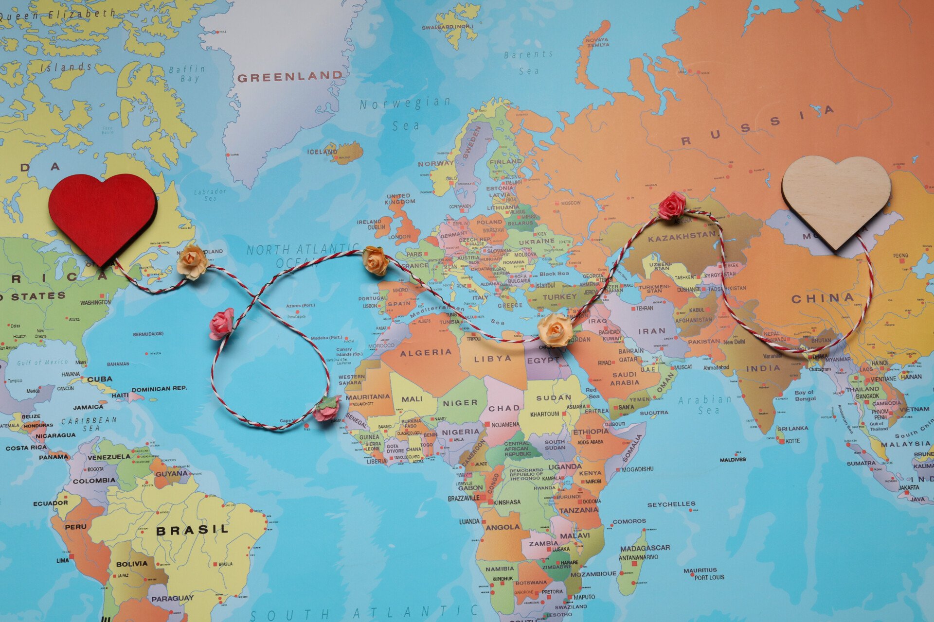 Decorative cord with hearts on world map symbolizing connection in long-distance relationship, top view