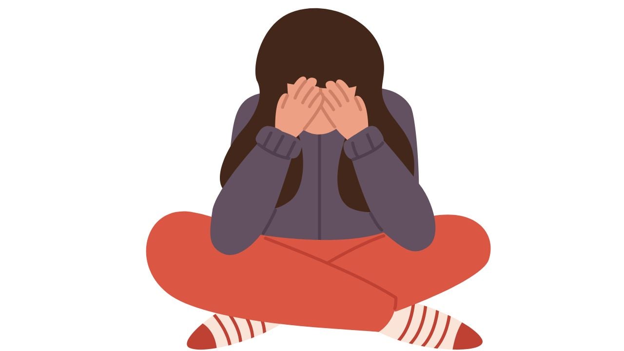 An adolescent girl sat cross-legged on the floor with head in her hands and feeling stressed.